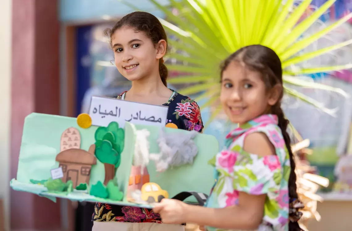 Haya (8 years old) and Haneem (10 years old) carrying an artwork on water conservation. Credit: UNICEF/UN0726815/Mostafa